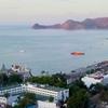 Vista costeira de Dili, Timor-Leste, mostrando um porto com um ferry e barcos na baía, e edifícios da cidade ao longo da orla marítima.