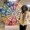 Profesa Smile Dzisi kutoka Ghana amesimama mbele ya gurudumu kubwa la SDG katika mkutano.