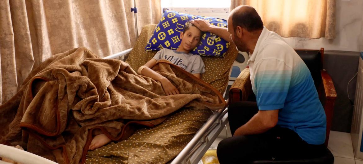 إبراهيم البنا يجلس بجانب ابنه كريم المصاب بجروح خطيرة، ويواسيه بعد أن أصيب بشظية بالقرب من كليته.