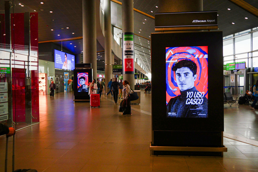 Un quiosco de publicidad digital para una campaña de seguridad vial se encuentra en una concurrida terminal de aeropuerto.