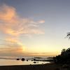 Una playa en Puerto Rico al atardecer, con olas, rocas, palmeras y un cielo colorido.