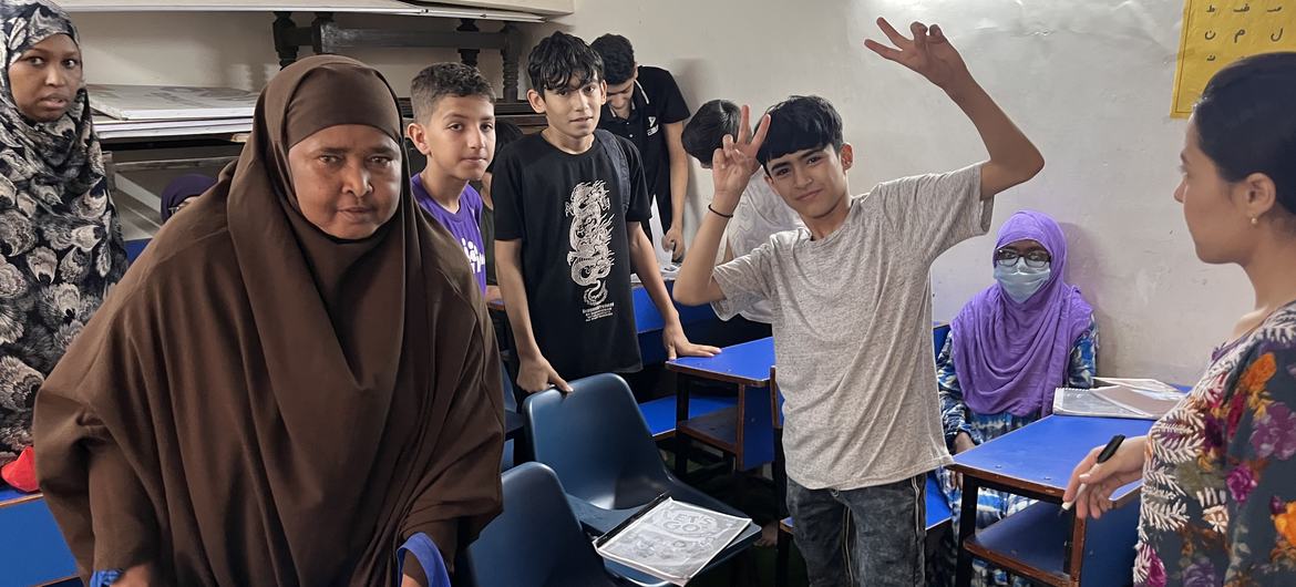 UNHCR इंडिया के एक कर्मचारी और छात्र कक्षा में बैठे हैं, जहां एक युवक शांति का चिन्ह बना रहा है।