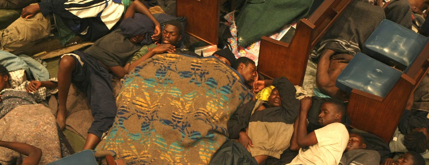 Des hommes dorment à même le sol de l'église méthodiste centrale de Johannesburg, utilisant les bancs comme appuie-tête. L'image montre une scène de foule de réfugiés cherchant un abri.