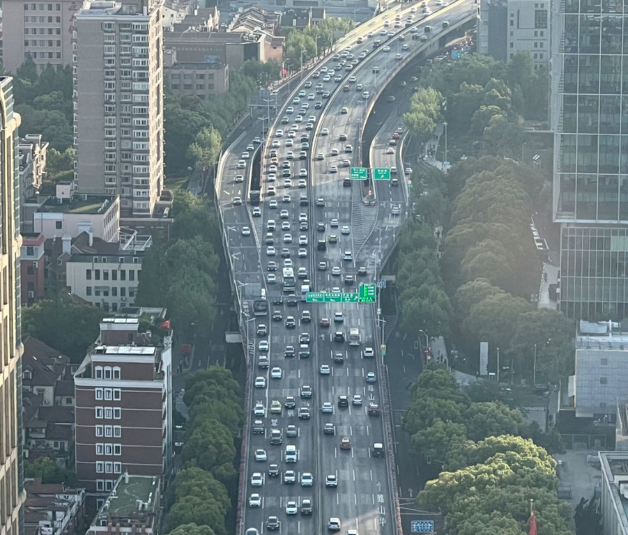 这是从空中俯瞰中国上海一条拥堵的多车道高速公路和立交桥的景象，繁忙的交通穿过人口密集的城市环境。