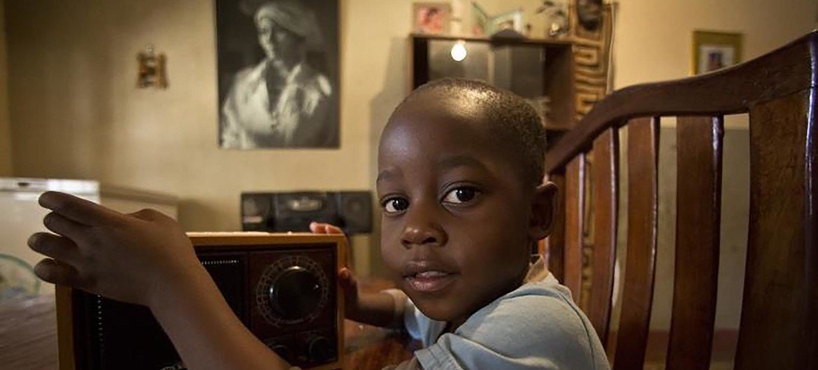 Um menino na República Democrática do Congo segura um rádio vintage, simbolizando transmissões educacionais durante a pandemia de COVID-19.