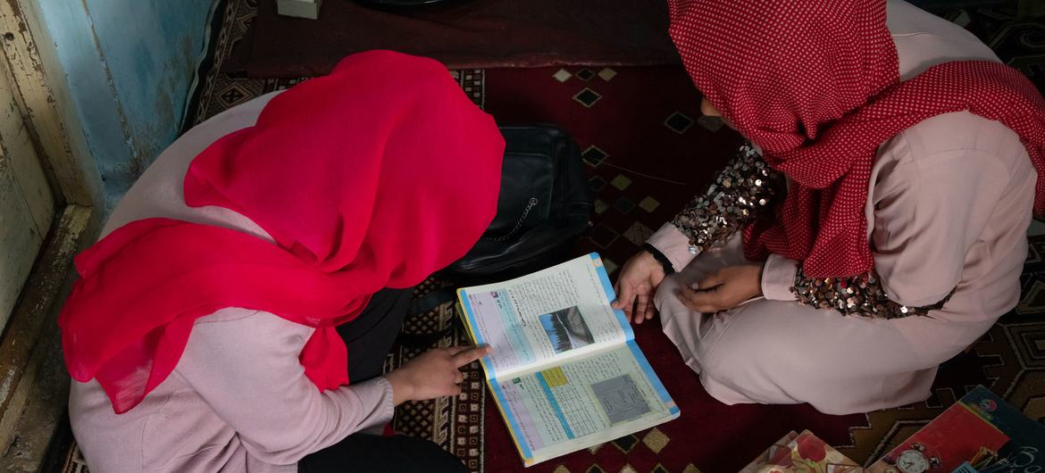 An Afghan girl studies at home with the help of her father after being denied the right to carry on studying at school. 