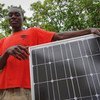 Kijana Mwafrika aliyevaa shati jekundu akiwa ameshika paneli ya jua inayotolewa na ILO huko Kasungu, Malawi.