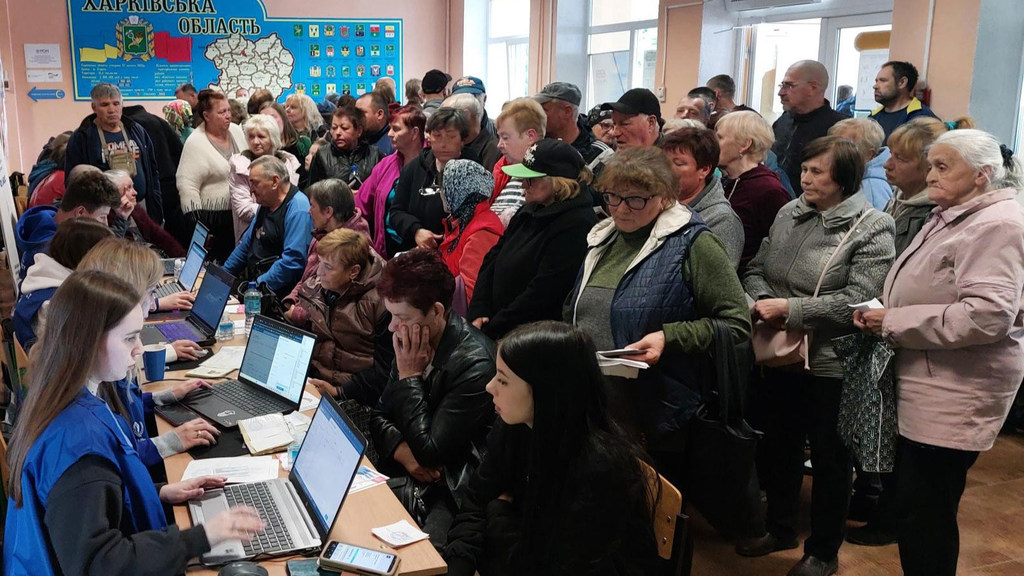 Personas desplazadas hacen fila en un mostrador de registro dentro de un centro de tránsito en Kharkiv, Ucrania, donde voluntarios les ayudan con las computadoras.