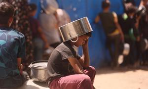 Un niño se pone una olla en la cabeza para protegerse del sol mientras espera para comer.