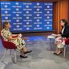 Ana Isabel Xavier é entrevistada por uma repórter em um estúdio de notícias com um grande painel da ONU News ao fundo.