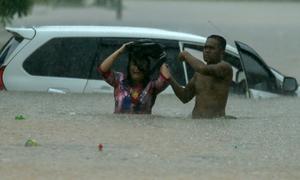 A man helps a woman after her car is stranded in waist-deep water. Globally rains are being more extreme due to impacts of climate change.