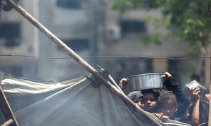 Tras una lona desgastada, niños de Gaza sostienen cuencos vacíos, con el rostro marcado por la fatiga y el hambre.