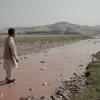 Um homem, identificado como Hidayatullah Sapi, está em pé no leito seco do Rio Vermelho, no leste do Afeganistão. A paisagem é árida, com montanhas ao longe.