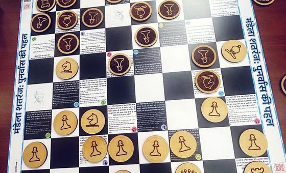 Picha ya karibu ya ubao wa kipekee wa chess ulioundwa na wafungwa wa zamani kwa ajili ya Ofisi ya UMOJA WA MATAIFA ya Dawa za Kulevya na Uhalifu (UNODC) nchini India, ukiwa na maudhui ya kielimu na alama za mageuzi ya magereza.