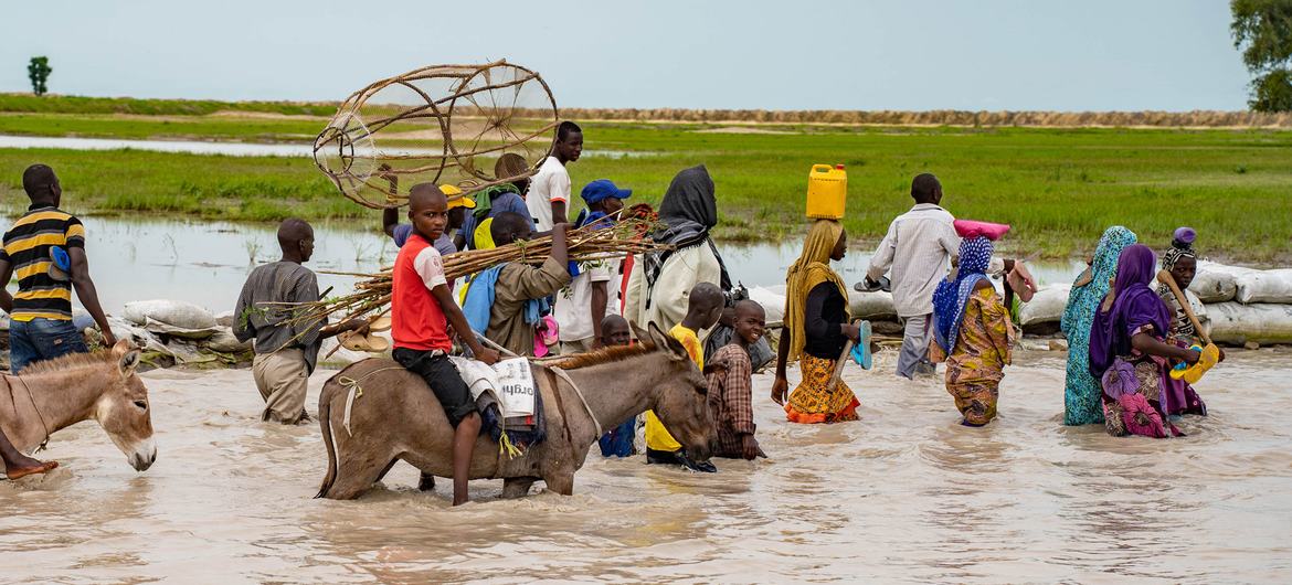 Residents of Rann, in north-east Nigeria, wade through the flooded main road, which is now inaccessible by vehicle.