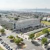 Vista aérea do campus do ISCTE-IUL em Lisboa, Portugal, com um edifício moderno e estacionamento, tendo a cidade e uma ponte como pano de fundo.