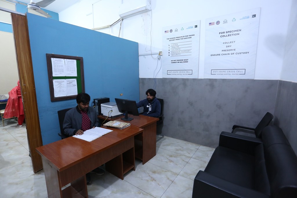 पाकिस्तान में बलात्कार विरोधी संकट प्रकोष्ठ के कार्यालय में दो पुरुष डेस्क पर बैठे हैं, जो यौन हिंसा से बचे लोगों को सहायता प्रदान कर रहे हैं और उनके दस्तावेजों को संसाधित कर रहे हैं।