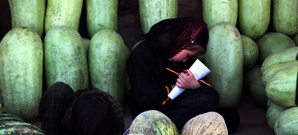 An Afghan girl snatches a moment away from her watermelon selling duties to work on her homework