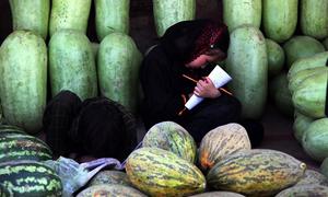 An Afghan girl snatches a moment away from her watermelon selling duties to work on her homework