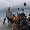 रोहिंज्या शरणार्थियों से भरी एक नाव, बांग्लादेश के टेकनाफ़ किनारे पर पहुँचने के बाद, एक व्यक्ति, एक महिला को किनारे तक पहुँचने में मदद करता हुआ. (फ़ाइल फ़ोटो)