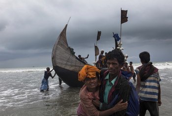 रोहिंज्या शरणार्थियों से भरी एक नाव, बांग्लादेश के टेकनाफ़ किनारे पर पहुँचने के बाद, एक व्यक्ति, एक महिला को किनारे तक पहुँचने में मदद करता हुआ. (फ़ाइल फ़ोटो)
