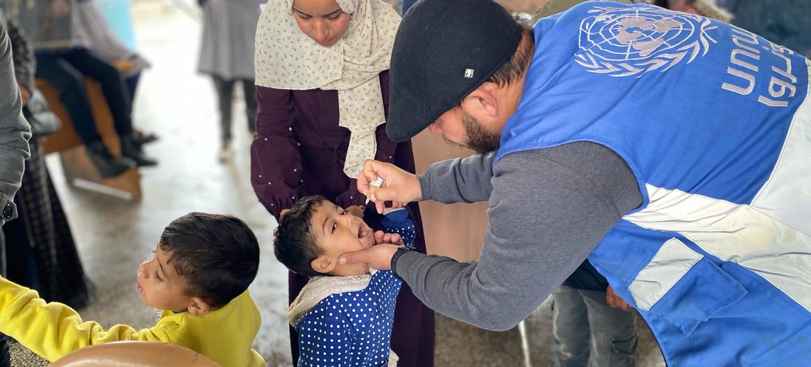 عاملة في وكالة الأونروا تعطي لقاح شلل الأطفال لطفل صغير في دير البلح، غزة.