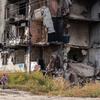 Um adulto e duas crianças passam por um bloco de apartamentos destruído em Borodianka, na Ucrânia.