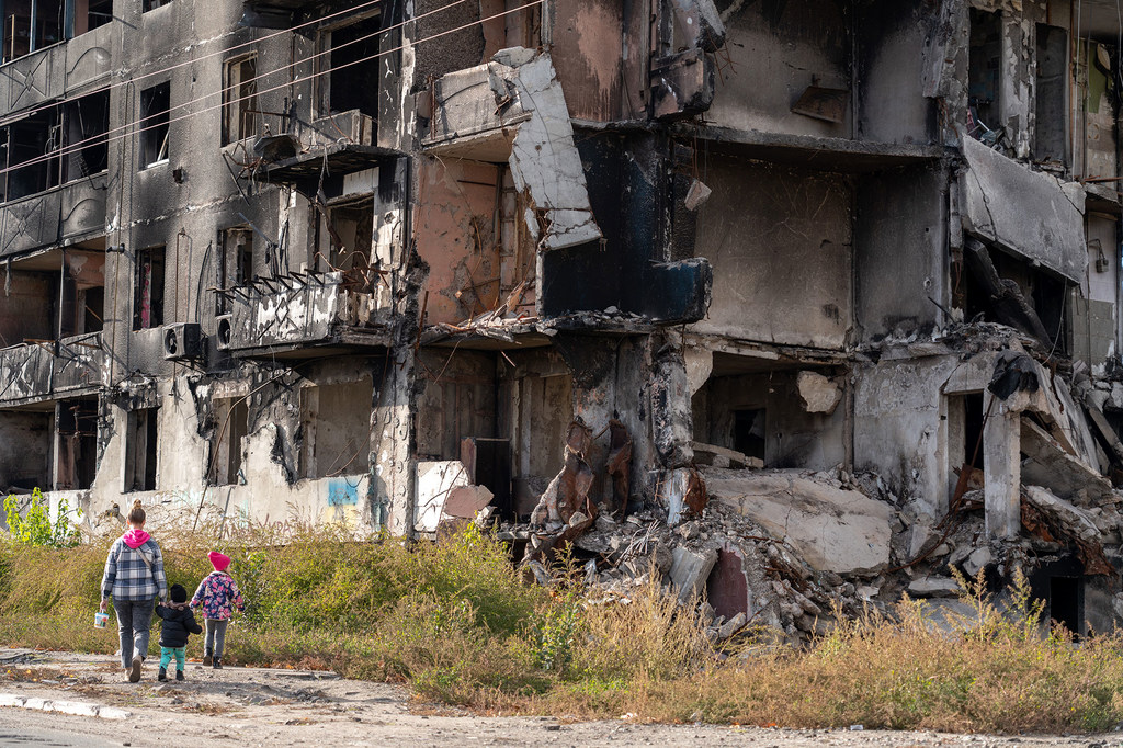 Una mujer y dos niños pasan junto a un edificio de apartamentos de varias plantas gravemente dañado en Borodianka, Ucrania, que ha sido destruido por ataques con misiles.