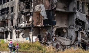 Um adulto e duas crianças passam por um prédio destruído em Borodianka, Ucrânia