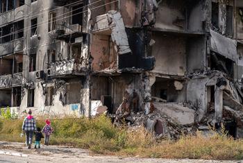 Um adulto e duas crianças passam por um prédio destruído em Borodianka, Ucrânia