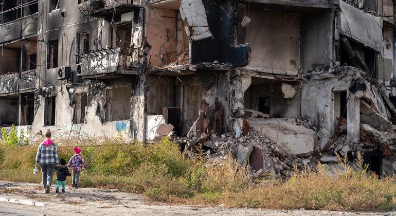 Um adulto e duas crianças passam por um bloco de apartamentos destruído em Borodianka, na Ucrânia.