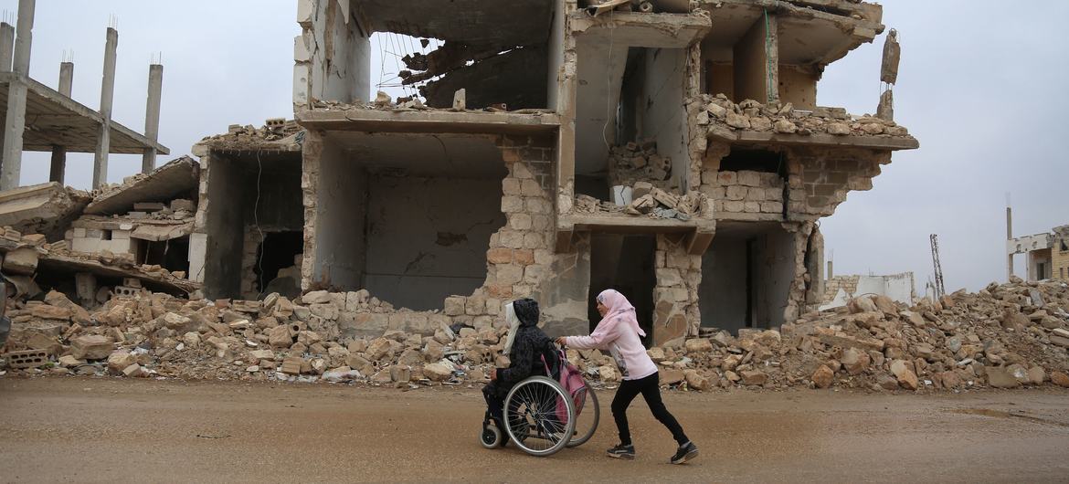 فتاة تدفع الكرسي المتحرك لشقيقتها أثناء عوتهما من المدرسة وسط الدمار في إدلب، شمال غرب سوريا.
