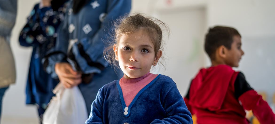 Una niña con un suéter azul sostiene una mochila escolar de UNICEF , con otros niños y adultos al fondo, en un acto de distribución en el sur del Líbano.