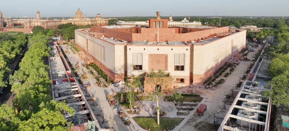 Uma vista aérea do edifício do Parlamento indiano em Nova Deli, mostrando sua arquitetura moderna e vegetação circundante.