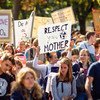 Une foule diversifiée de jeunes défile pacifiquement pour le climat, brandissant des pancartes avec des messages tels que « Faites l'amour, pas du CO2 » et « Respectez votre mère ».