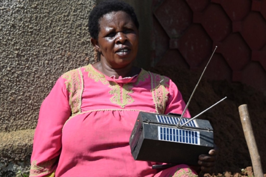 Kavira Vakekya, mkazi wa Beni, DRC, anashikilia redio inayotumia nishati ya jua mbele ya jengo.