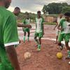 Jogadores de futebol angolanos com uniformes verdes e brancos em um campo enlameado.