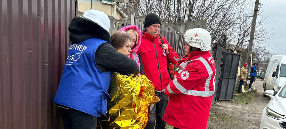 Медицинский персонал и сотрудники гуманитарных организаций в Украине оказывают помощь женщине, завернутой в золотистое термоодеяло, после недавнего нападения в Днепре.