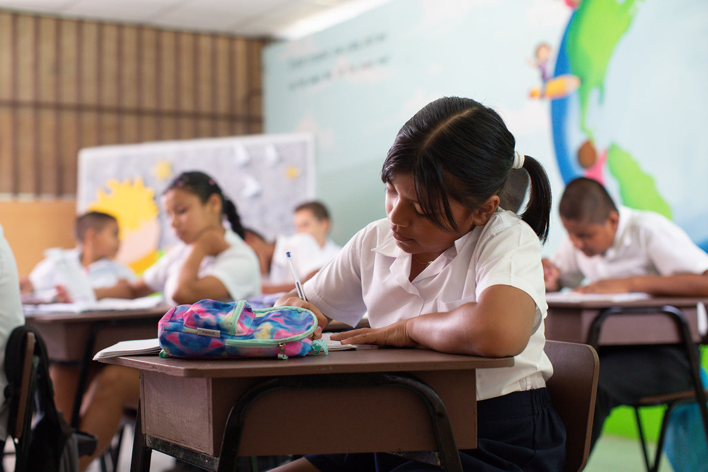 Una joven estudiante con uniforme blanco toma apuntes en su cuaderno durante una clase en la escuela Vegas de Río Palacios en Limón, Costa Rica.