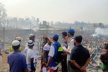 बांग्लादेश के कुटुपलोंग शरणार्थी शिविर में, आग लगने के बाद नुक़सान का जायज़ा लेते, आईओएम के सहायताकर्मी. पृष्ठभूमि में, आग से विस्थापित हुए शरणार्थी नज़र आ रहे हैं.