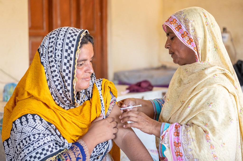 ایک پاکستانی خاتون صحت کی دیکھ بھال کرنے والے کارکن سے ویکسین حاصل کر رہی ہے۔