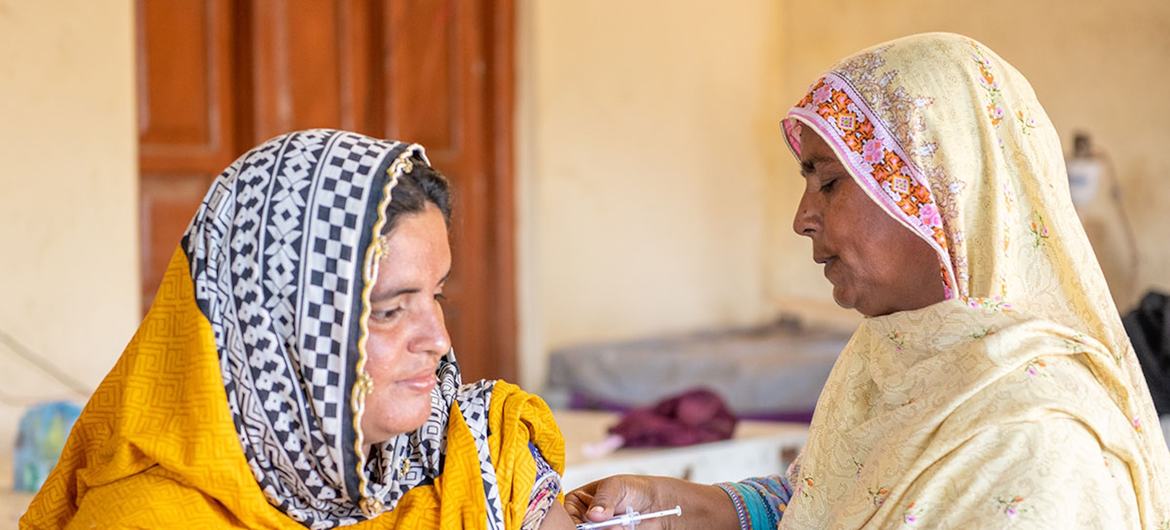 ایک پاکستانی خاتون صحت کی دیکھ بھال کرنے والے کارکن سے ویکسین حاصل کر رہی ہے۔