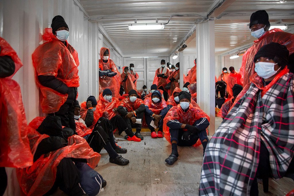 Les survivants migrants portant des imperméables rouges et des masques se trouvent à bord d'un navire de sauvetage après avoir été secourus en mer.
