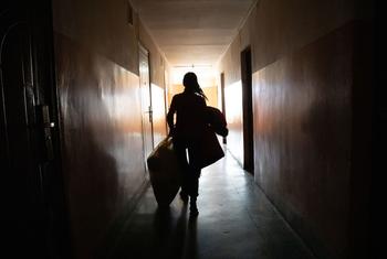 Uma pessoa em silhueta carrega malas com pertences por um corredor pouco iluminado em um dormitório universitário na Ucrânia.