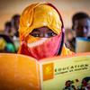 Uma jovem maliana com um lenço amarelo e vermelho na cabeça lê um livro didático em uma sala de aula em Kidal, Mali.