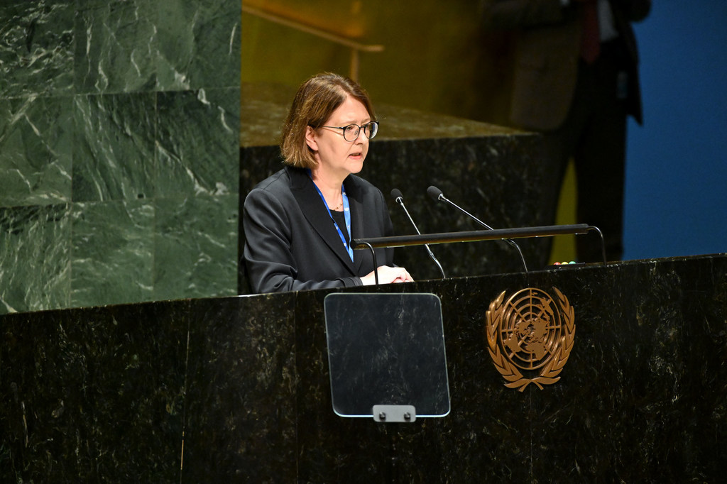 जर्मन राजदूत एंटजे लीनडर्टसे UN महासभा के एक सत्र के दौरान United Nations के प्रतीक चिन्ह वाले मंच पर भाषण दे रही हैं।