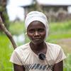 Amina Hakizimana, mwanamke kutoka Burundi, anaangalia kamera. Amevaa kitambaa cheupe kichwani na fulana yenye kipaza sauti, akiwa amesimama kwenye uwanja uliojaa maji.