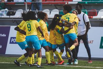 A seleção feminina juvenil do Brasil comemora com um abraço coletivo em campo durante uma partida.