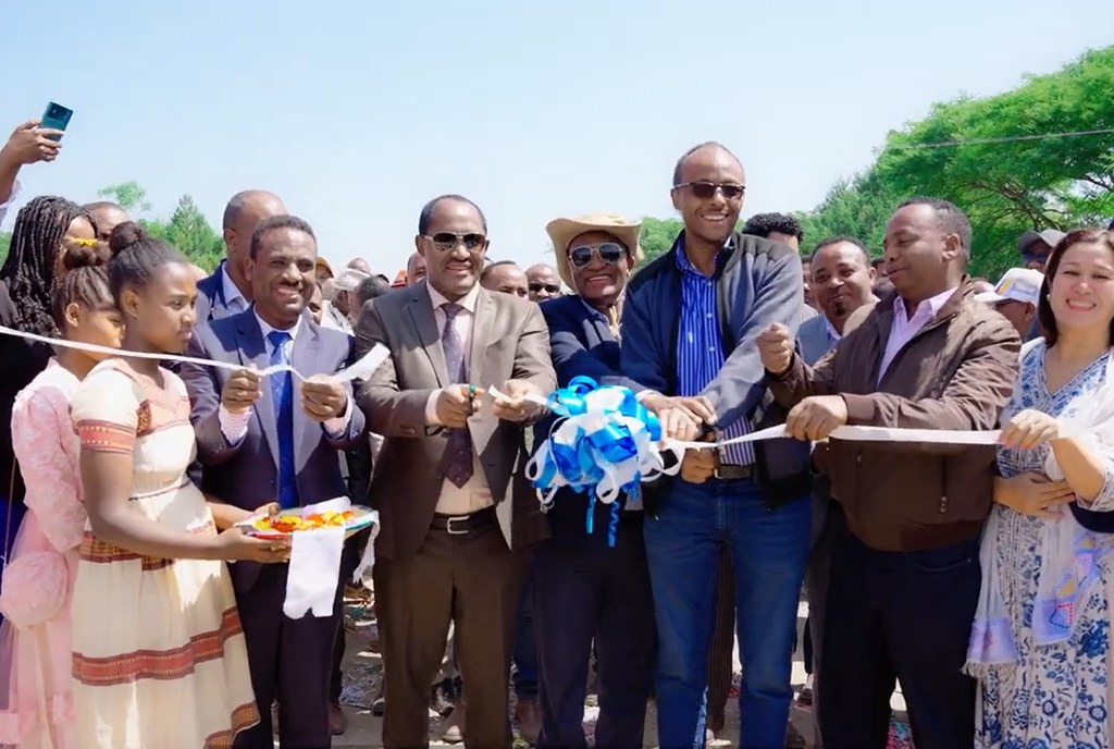 Kundi la wanaume na wanawake waliovalia mavazi rasmi na ya kitamaduni wakikata utepe wakati wa sherehe ya uzinduzi wa nje.
