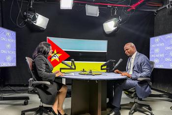 Uma repórter entrevista um homem em um estúdio com a marca ONU News e as bandeiras das Nações Unidas e de Moçambique ao fundo.